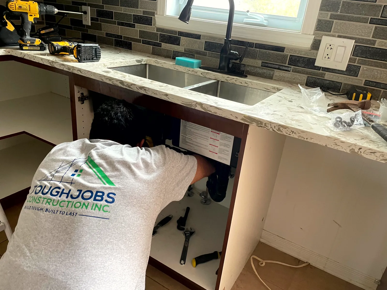 A ToughJobs crew member in a branded company shirt installing a kitchen sink on a Greater Montreal job site