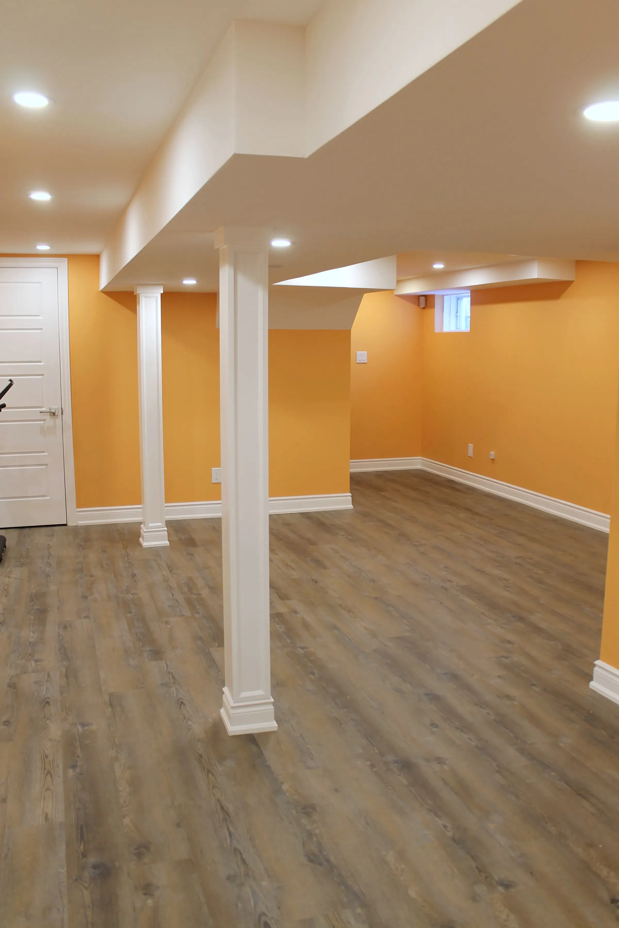 Finished open basement with orange walls, white columns and a bulkhead by ToughJobs Construction