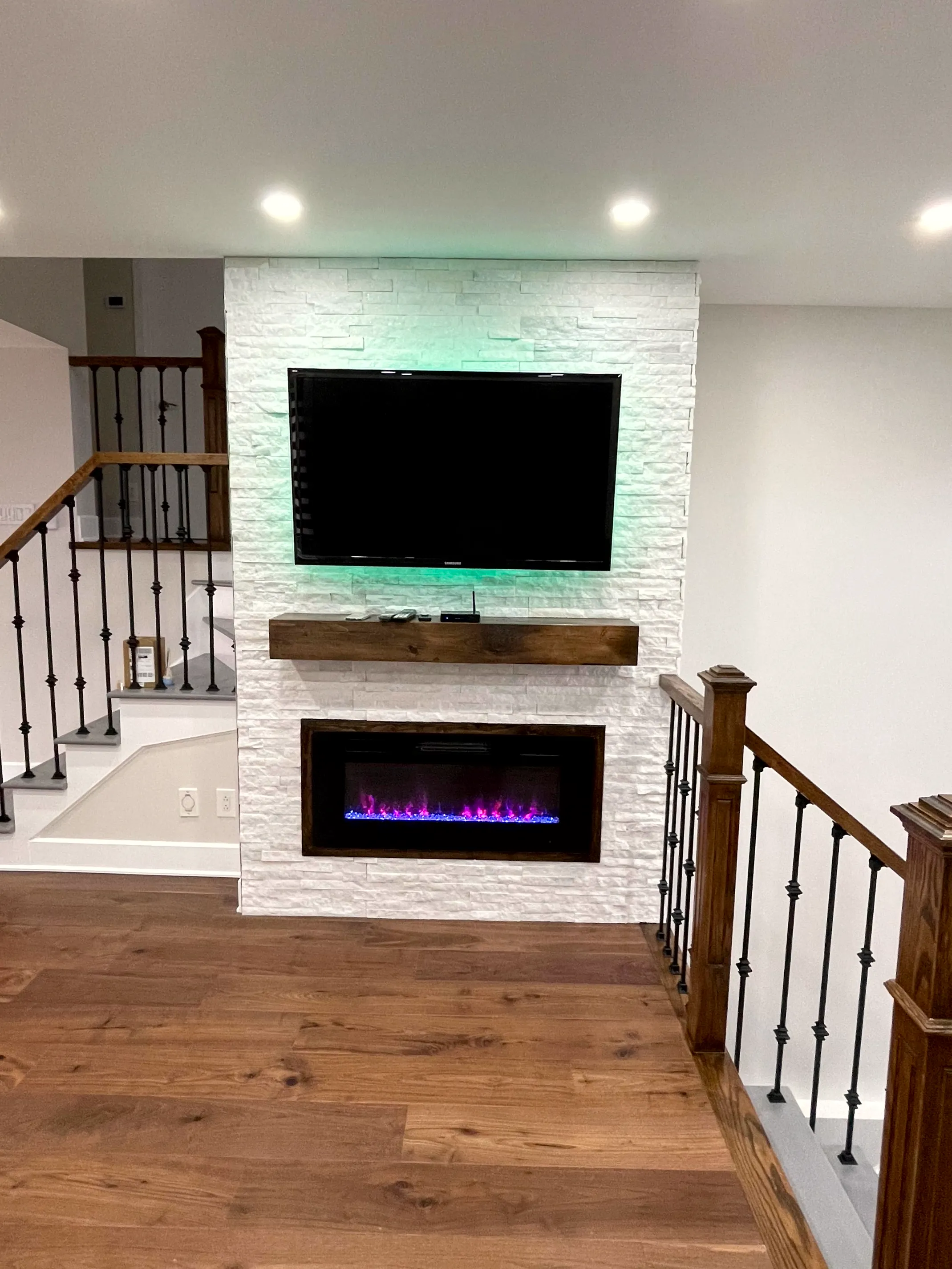 Finished basement media wall in white stacked stone with a mounted TV and linear fireplace by ToughJobs