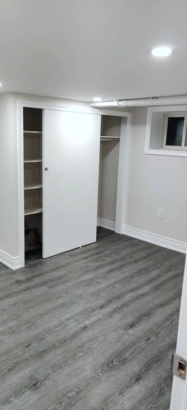Finished basement bedroom with grey wood-look plank floor, a sliding closet door, recessed lighting, white baseboards, and a small window.