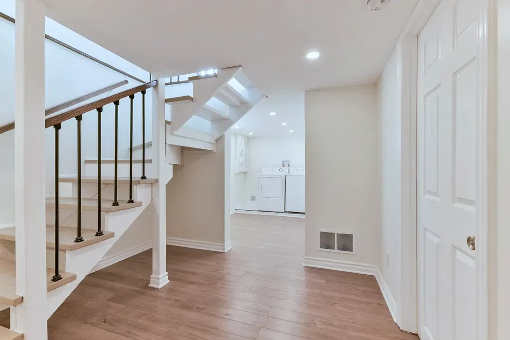Finished basement with a modern open staircase, iron balusters, laminate flooring, recessed lighting, and a laundry area.