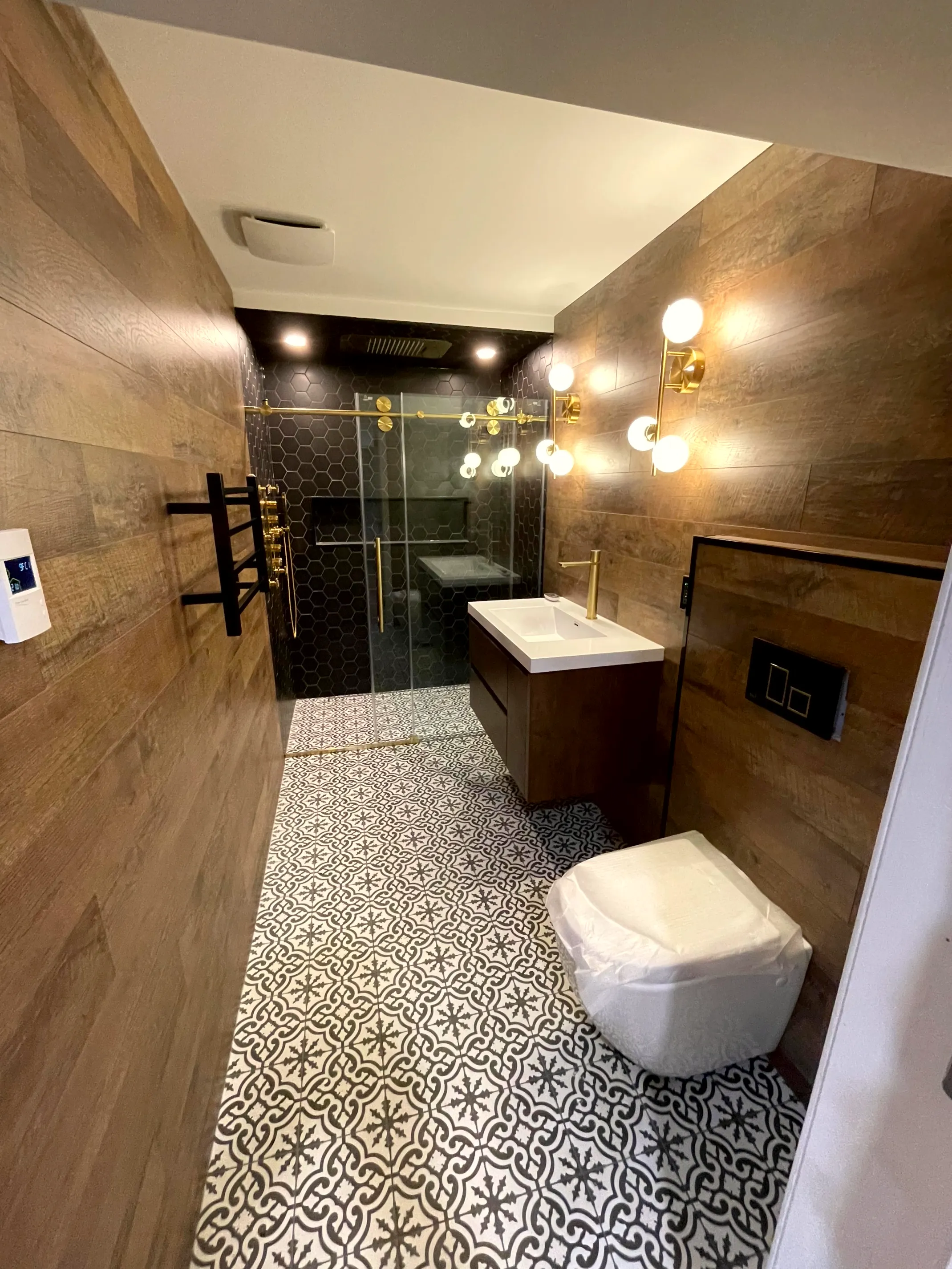 Finished bathroom with wood-look wall tile, glass shower, vanity with a vessel sink, and patterned floor tile.