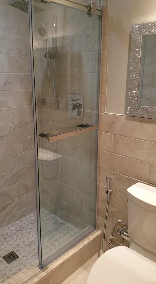 Finished walk-in shower, beige stone-look wall tile, mosaic floor, sliding glass enclosure, chrome handheld on a slide bar.