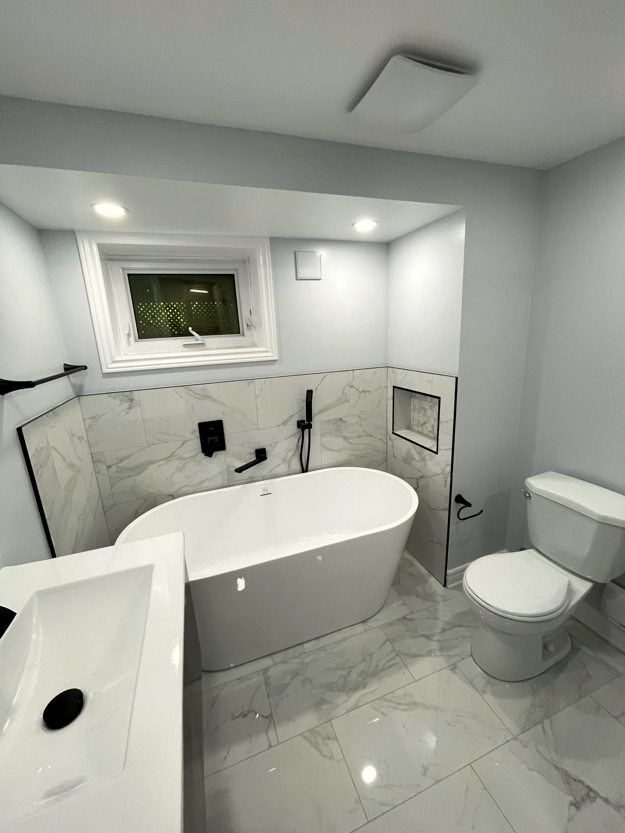 Finished basement bathroom with a freestanding tub, marble-look porcelain walls, a glass walk-in shower, and matte black fixtures.