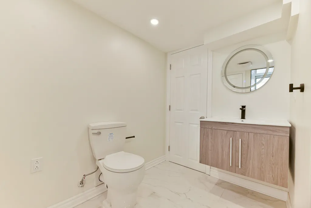 Finished basement powder room with a wood-look floating vanity, round mirror, matte black fixtures, and stone-look floor tile.