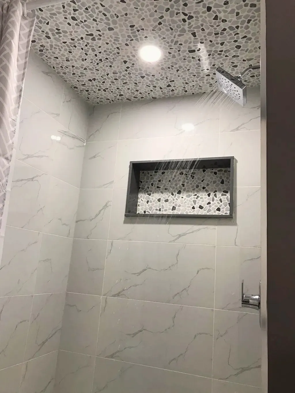 Finished walk-in shower with light wall tile, a pebble-mosaic ceiling and matching niche, and a chrome rainhead.