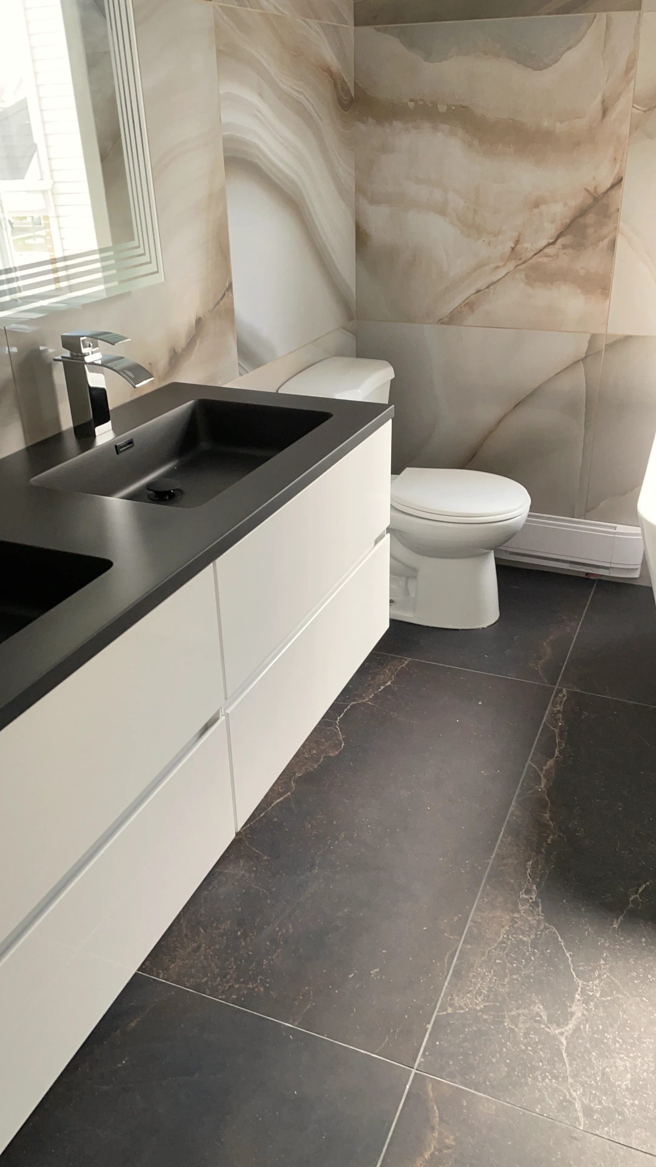 Finished bathroom with a white floating vanity, dark stone-look counter, stone-look wall panel, toilet, and dark floor tile.