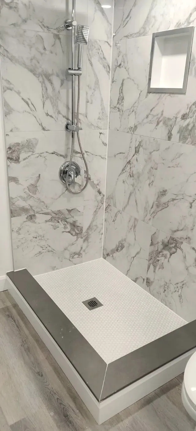 Finished walk-in shower with stone-look wall tile, chrome rainhead and handheld, recessed niche, and penny-round floor pan.