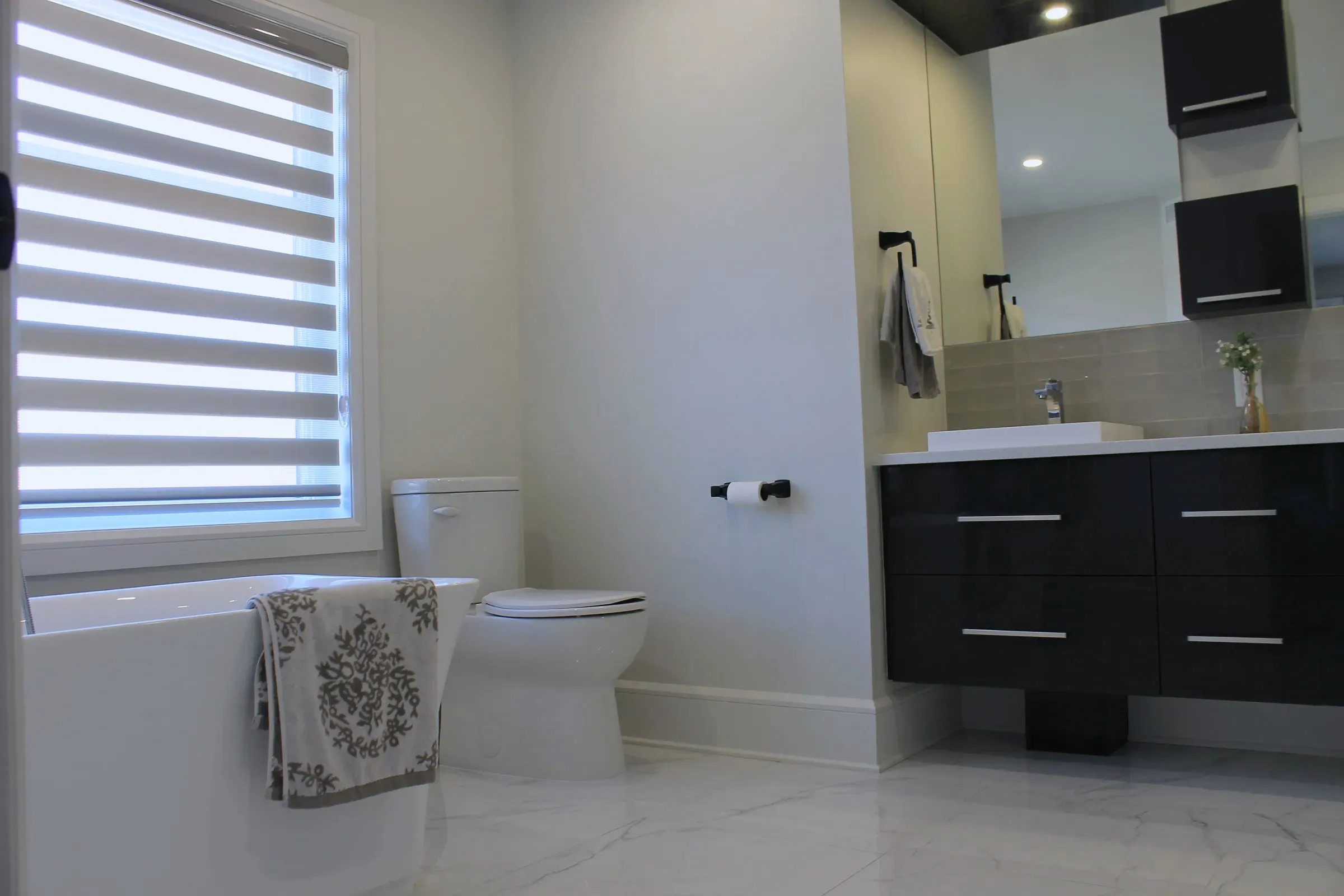 Finished bathroom with an alcove tub, a dark floating vanity with vessel sink, large mirror, and stone-look floor tile.