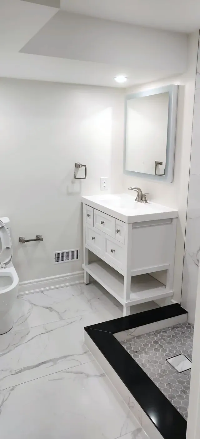 Finished basement bathroom with white vanity, stone-look floor tile, toilet, and a corner shower base with hex mosaic.