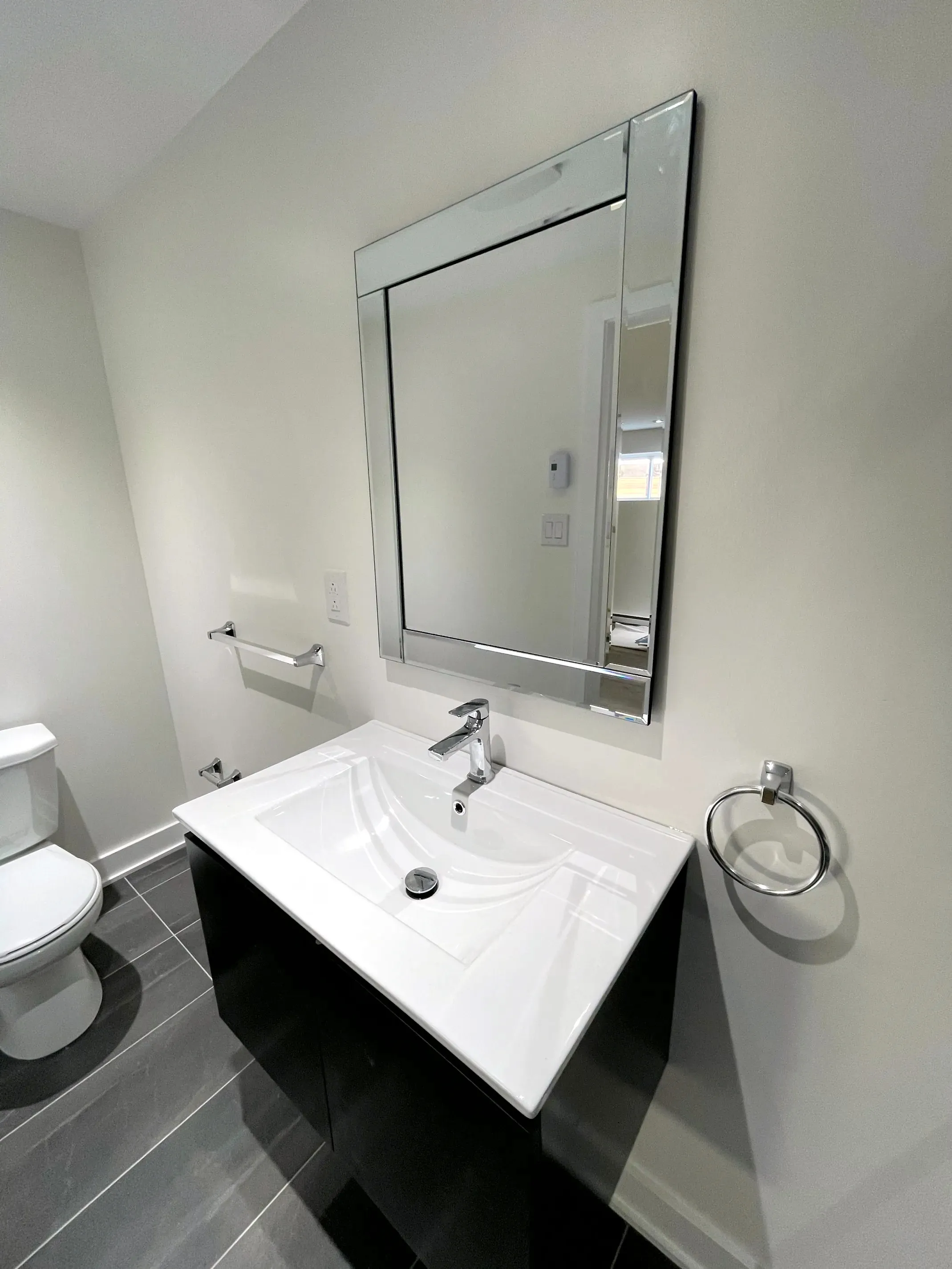 Finished half bath, black floating vanity, white sink, framed mirror, chrome towel ring and dark grey floor tile.