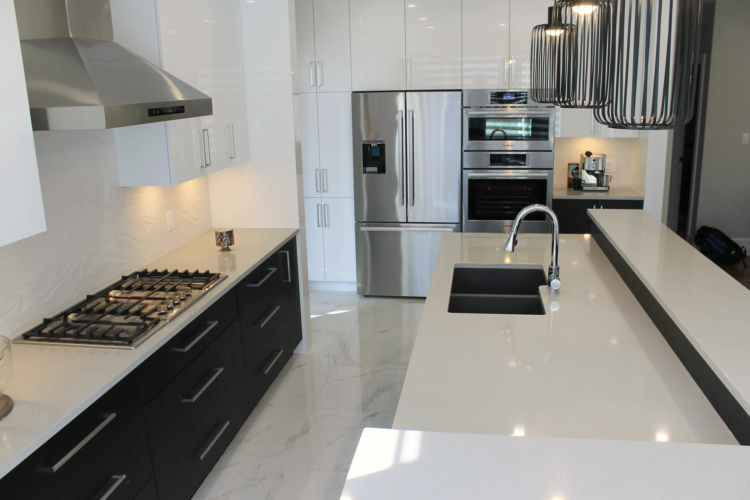 Finished kitchen with white upper cabinets, dark lowers, stainless hood, gas cooktop, double wall oven, and stone-look floor.