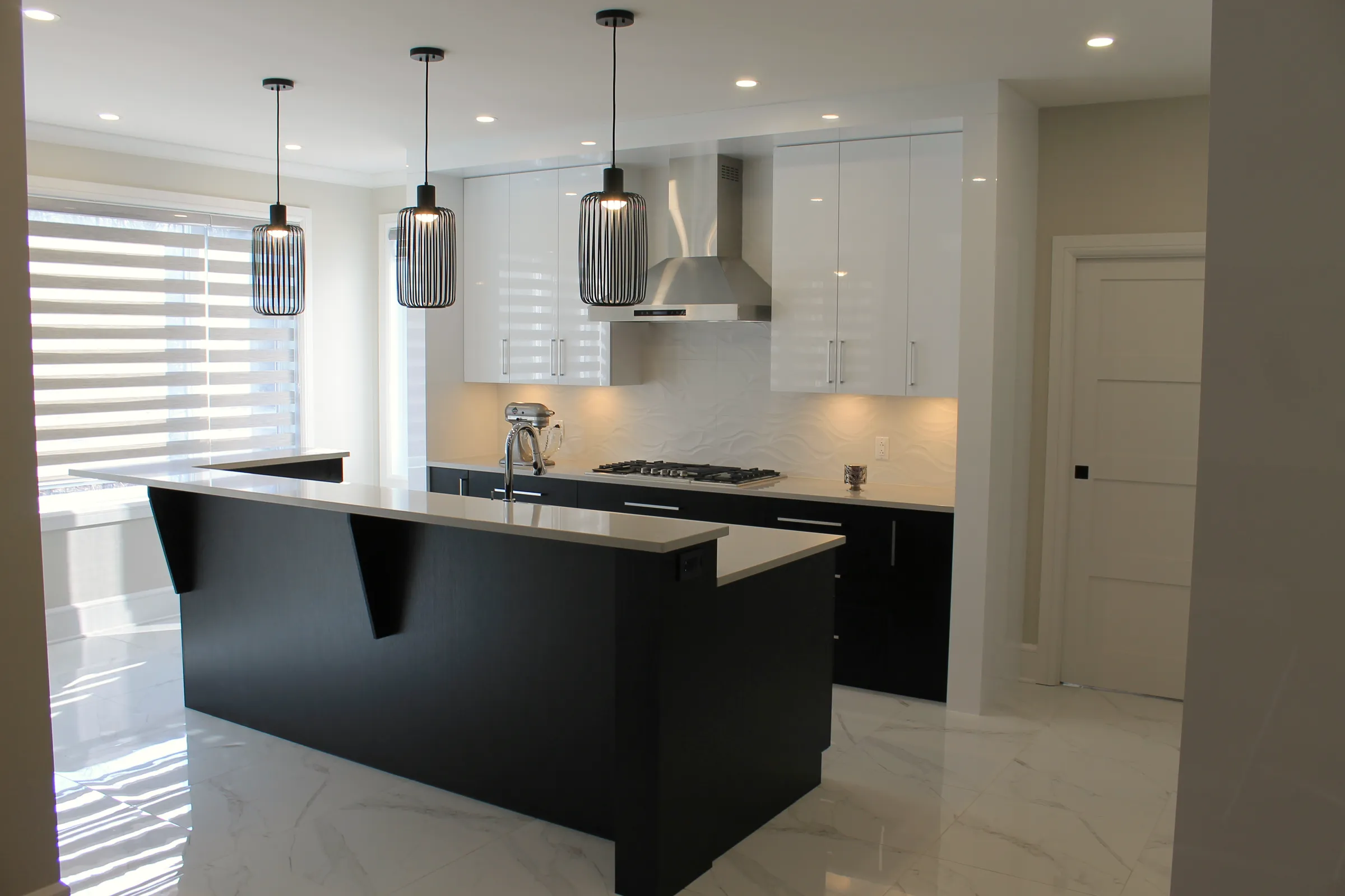 Finished kitchen with white cabinets, dark island, stainless hood, gas cooktop, three black cage pendants, and stone-look floor.