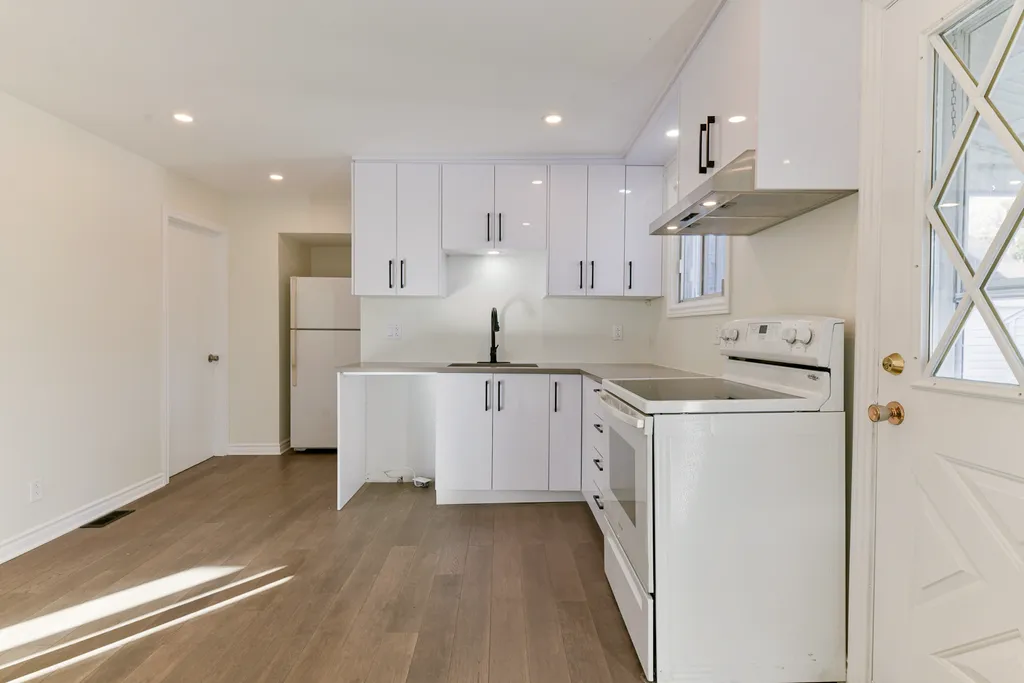Finished compact kitchen with white cabinets, black hardware, white range and fridge, and wood-look floor.
