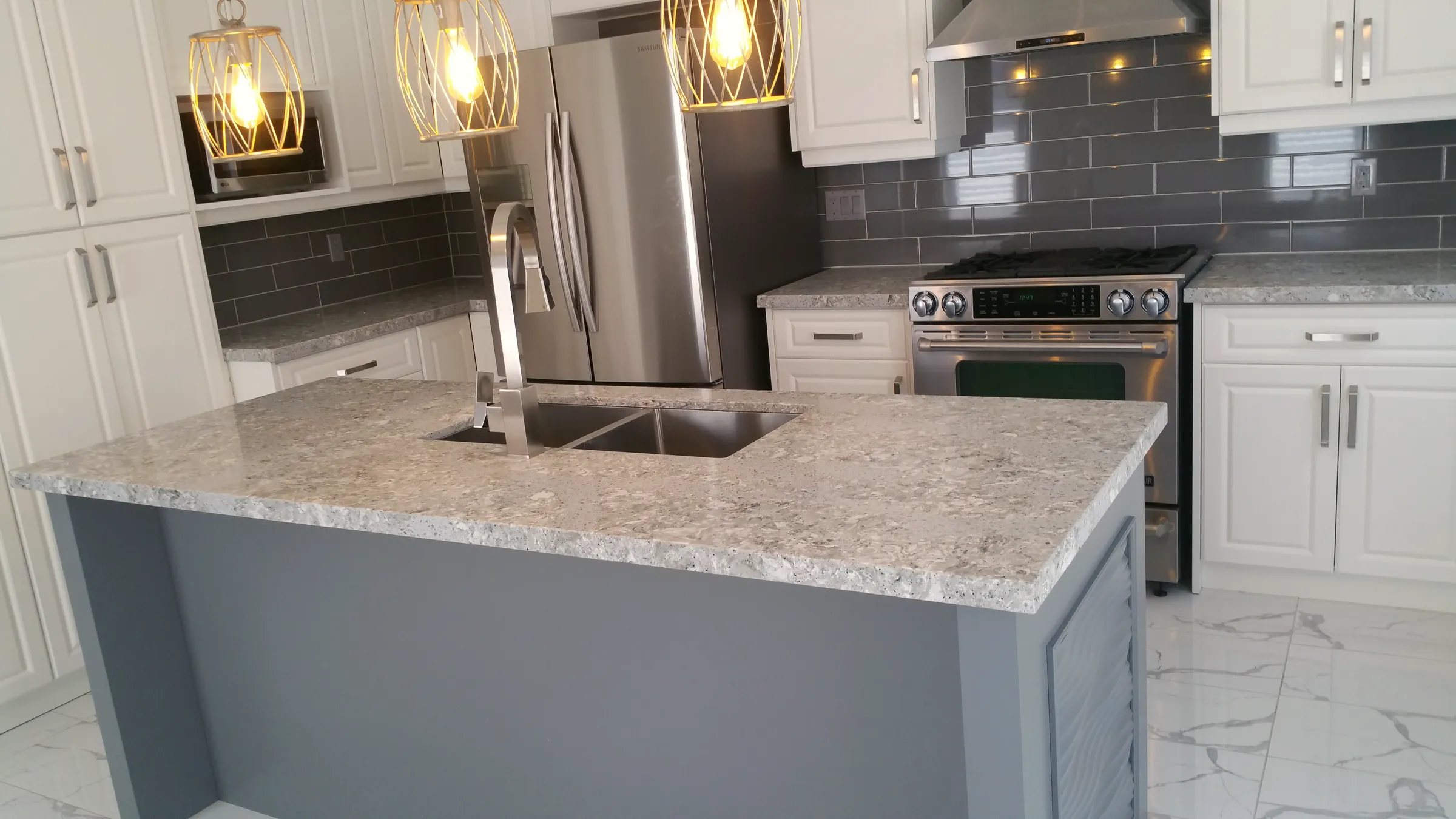 Finished kitchen island with grey base, stone-look counter, undermount double sink, stone-look floor, and stainless appliances.