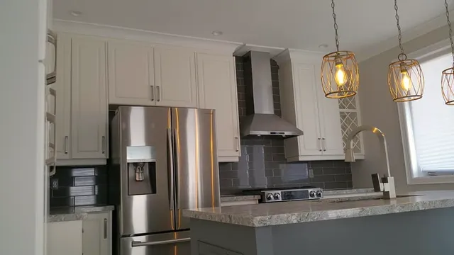 Finished kitchen with white cabinets, grey wall-tile backsplash, stone-look counters, stainless chimney hood, and cage pendants over a grey island.