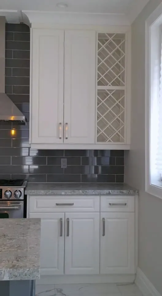 Finished kitchen detail with a built-in wine lattice rack, white cabinets, stone-look counters, and grey wall-tile backsplash.