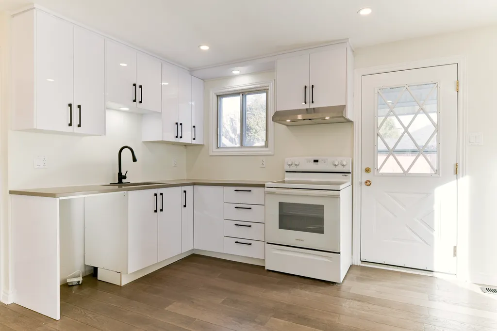 Finished kitchen with white cabinets, black hardware, black faucet, white range, and wood-look floor.