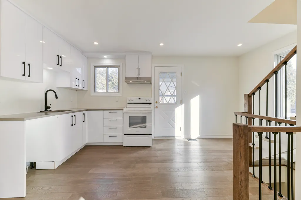 Finished kitchen with white cabinets, black hardware, black faucet, white range, wood-look floor, and a wood-and-iron staircase.