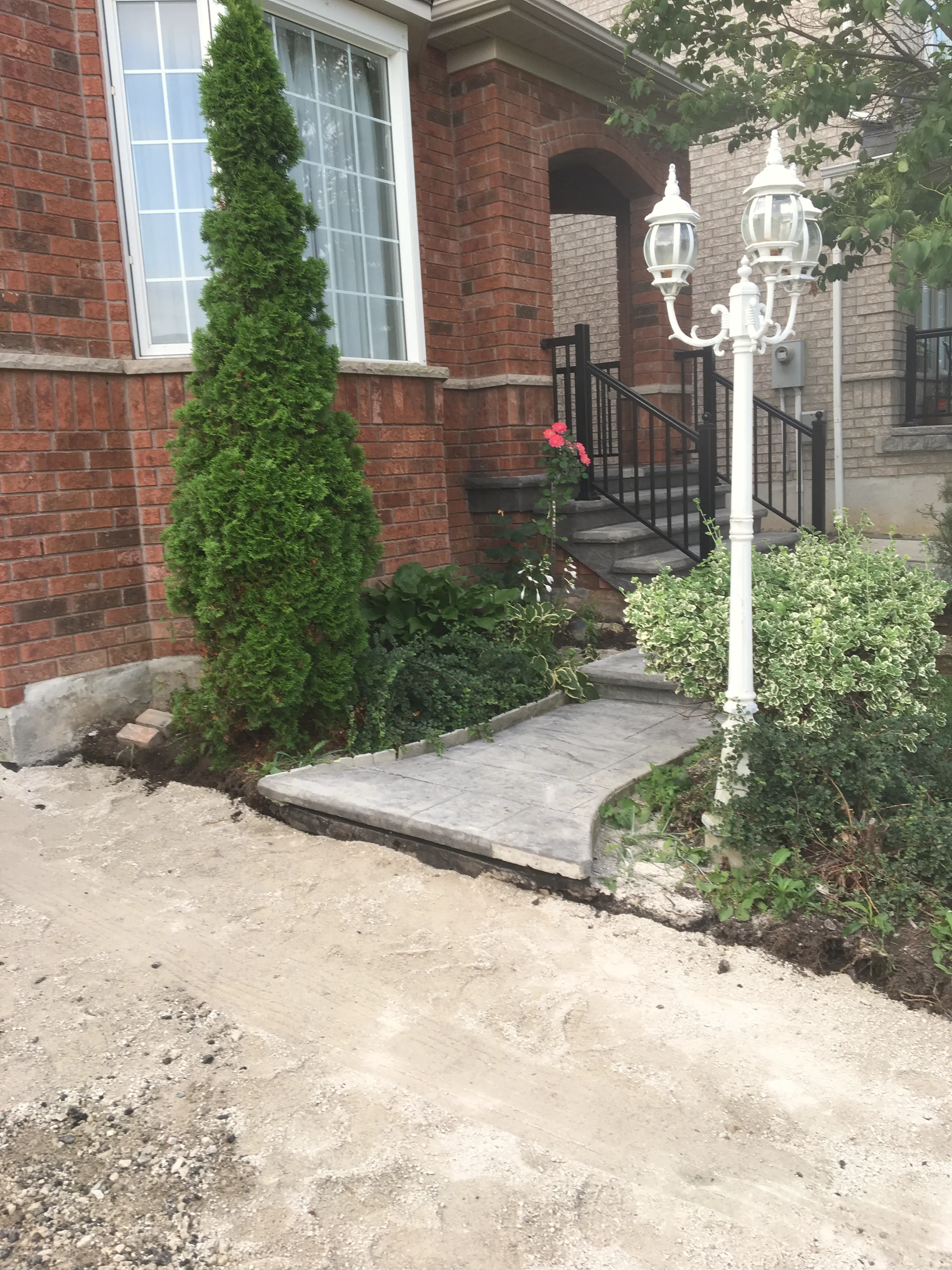 Stone-paver front walkway and steps with a black metal railing beside the brick house.