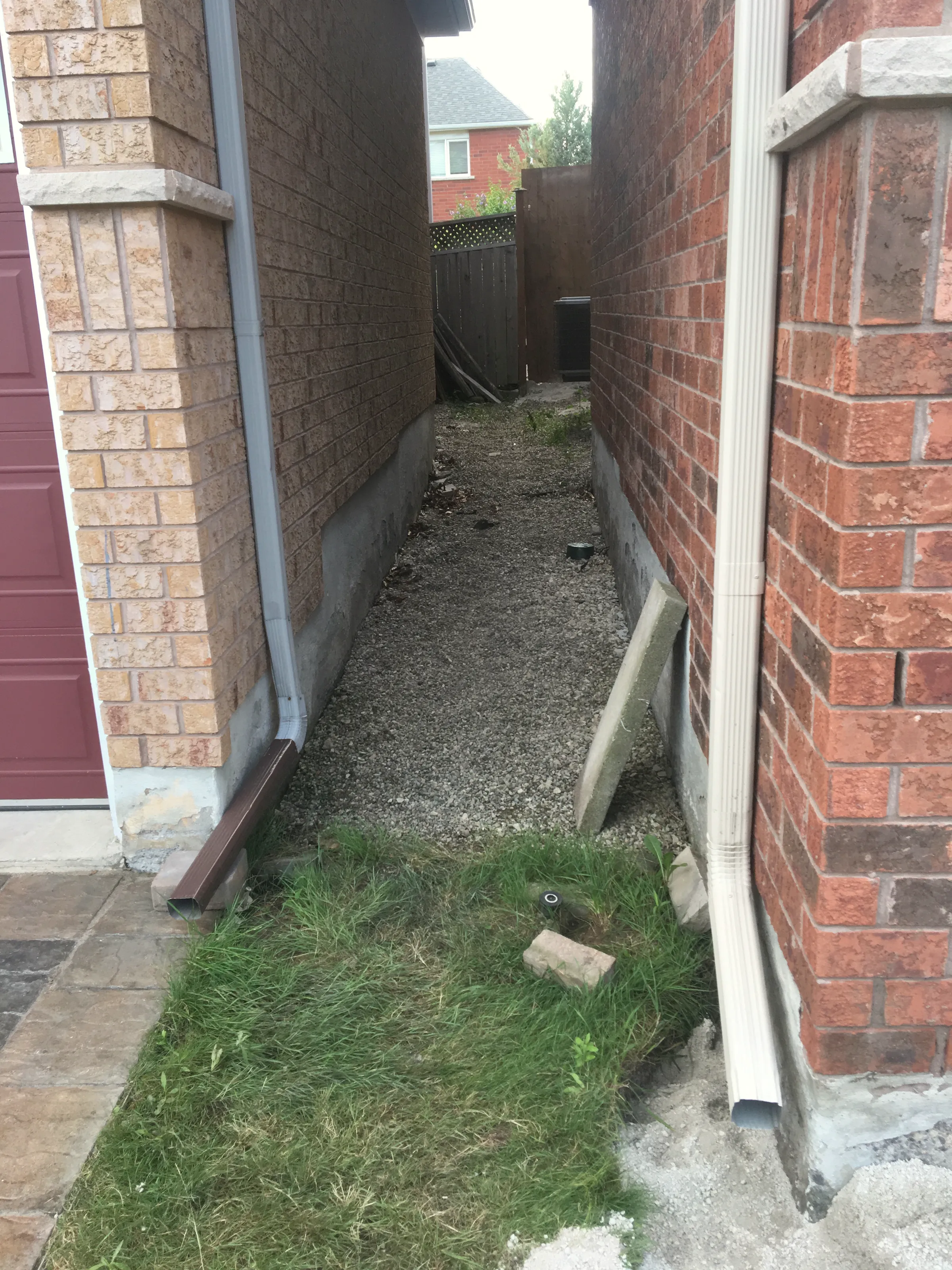 Gravel side yard between two brick houses with downspouts draining to grade.
