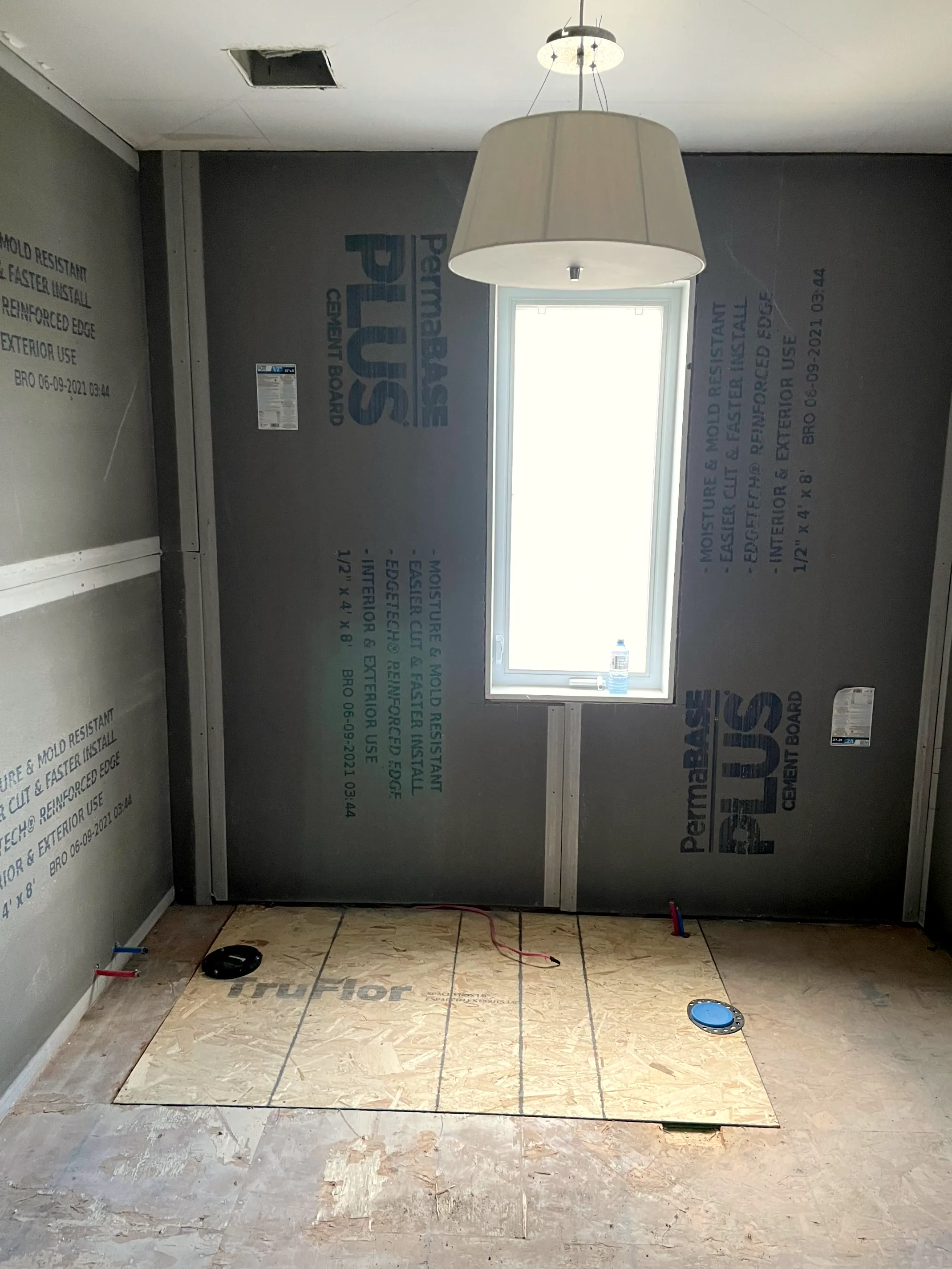 Bathroom with cement-board walls, a window, subfloor panels down, and a pendant light overhead.