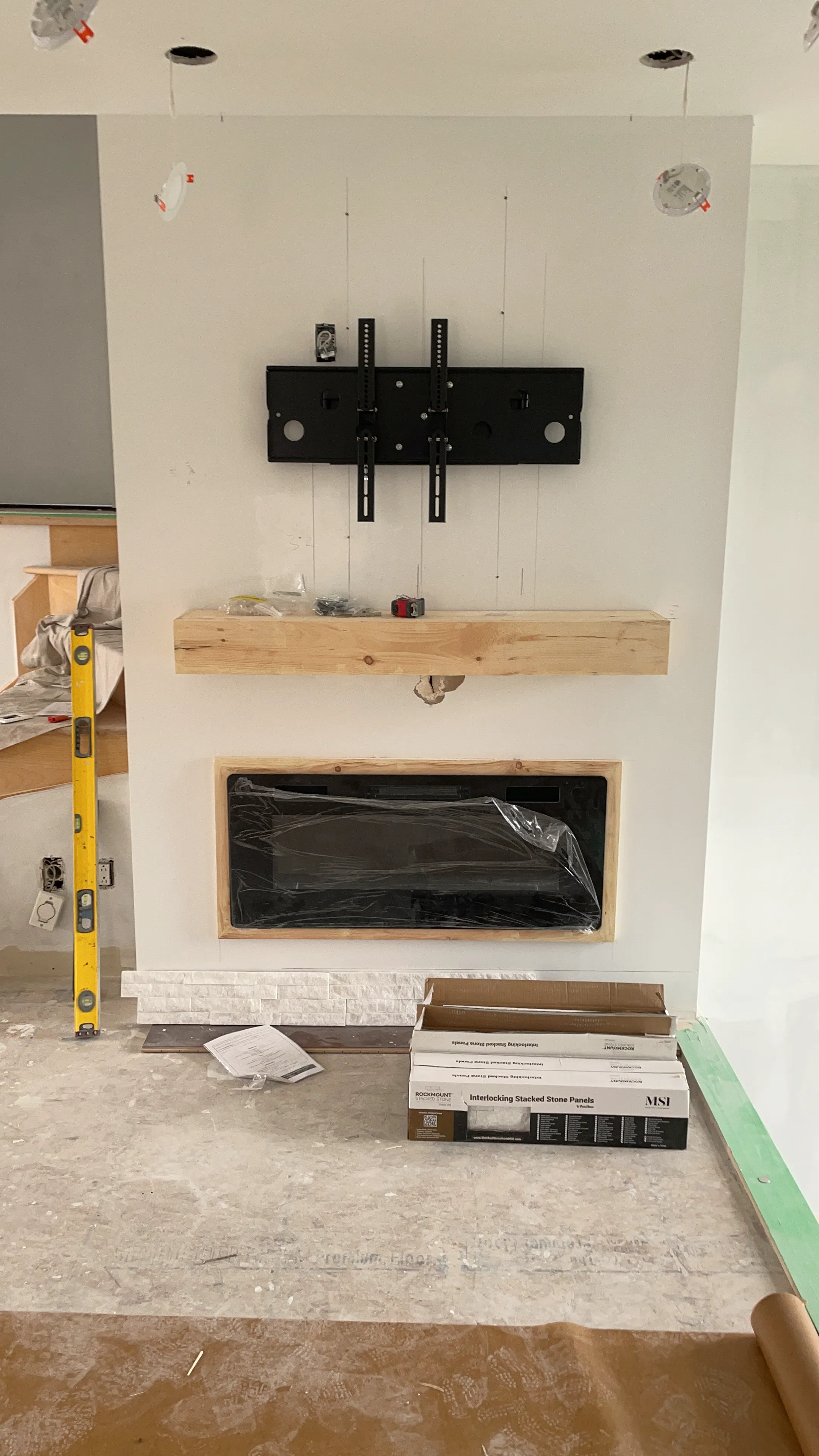 Fireplace wall with a TV mount bracket, a wood mantel, and stone panels at the base.