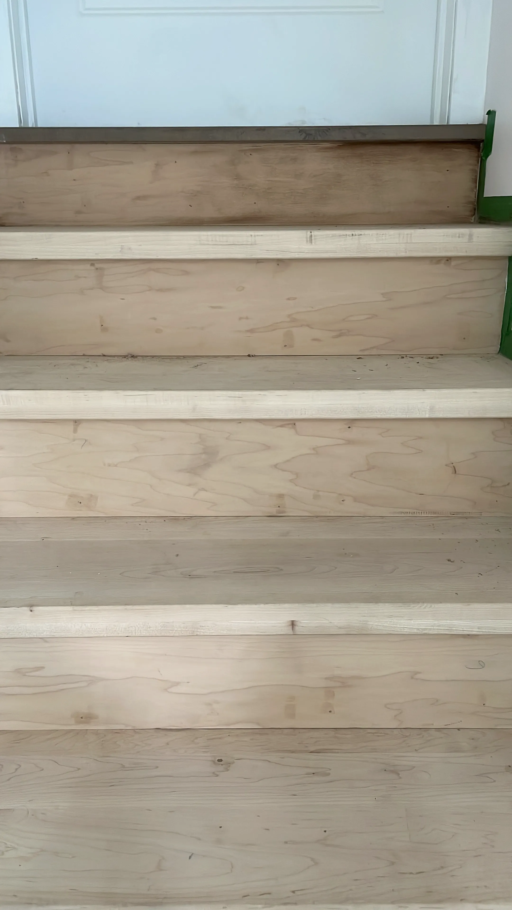 New light wood stair treads and risers installed, with green tape along the side wall.