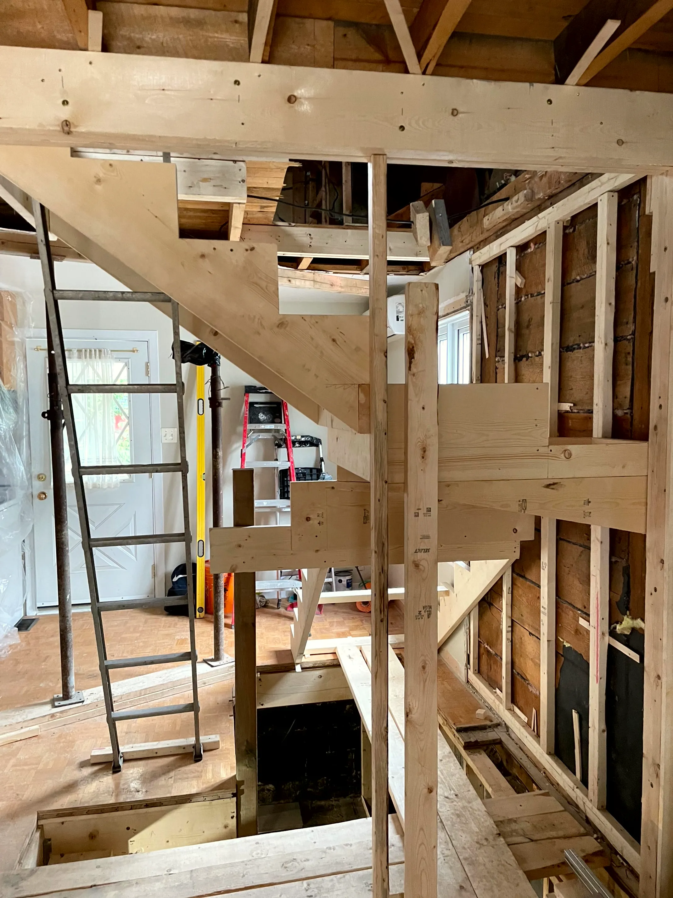 New wood stair framing inside a gutted house, exposed studs around it and a ladder for access.