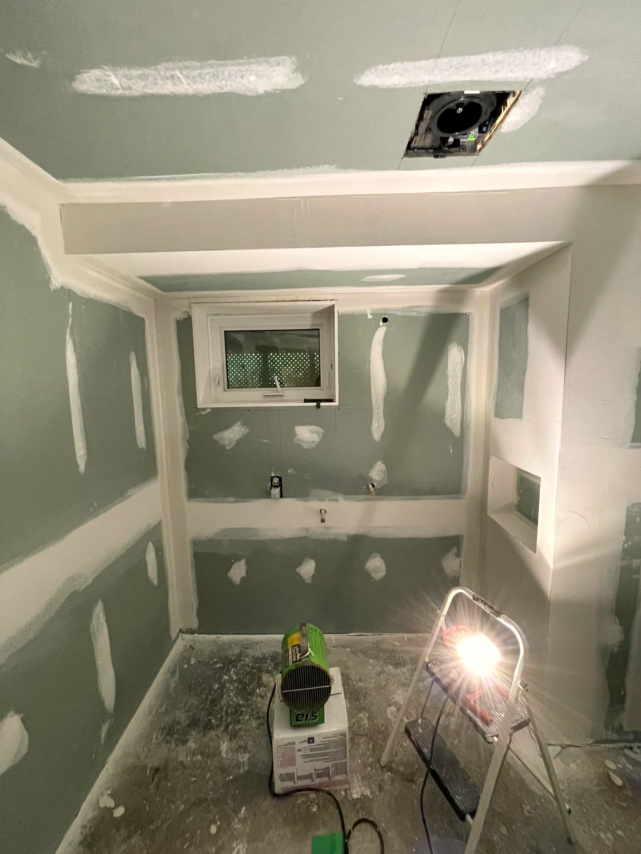 Drywalled bathroom with taped joints, a small window, ceiling fan, recessed niche, and a work light.