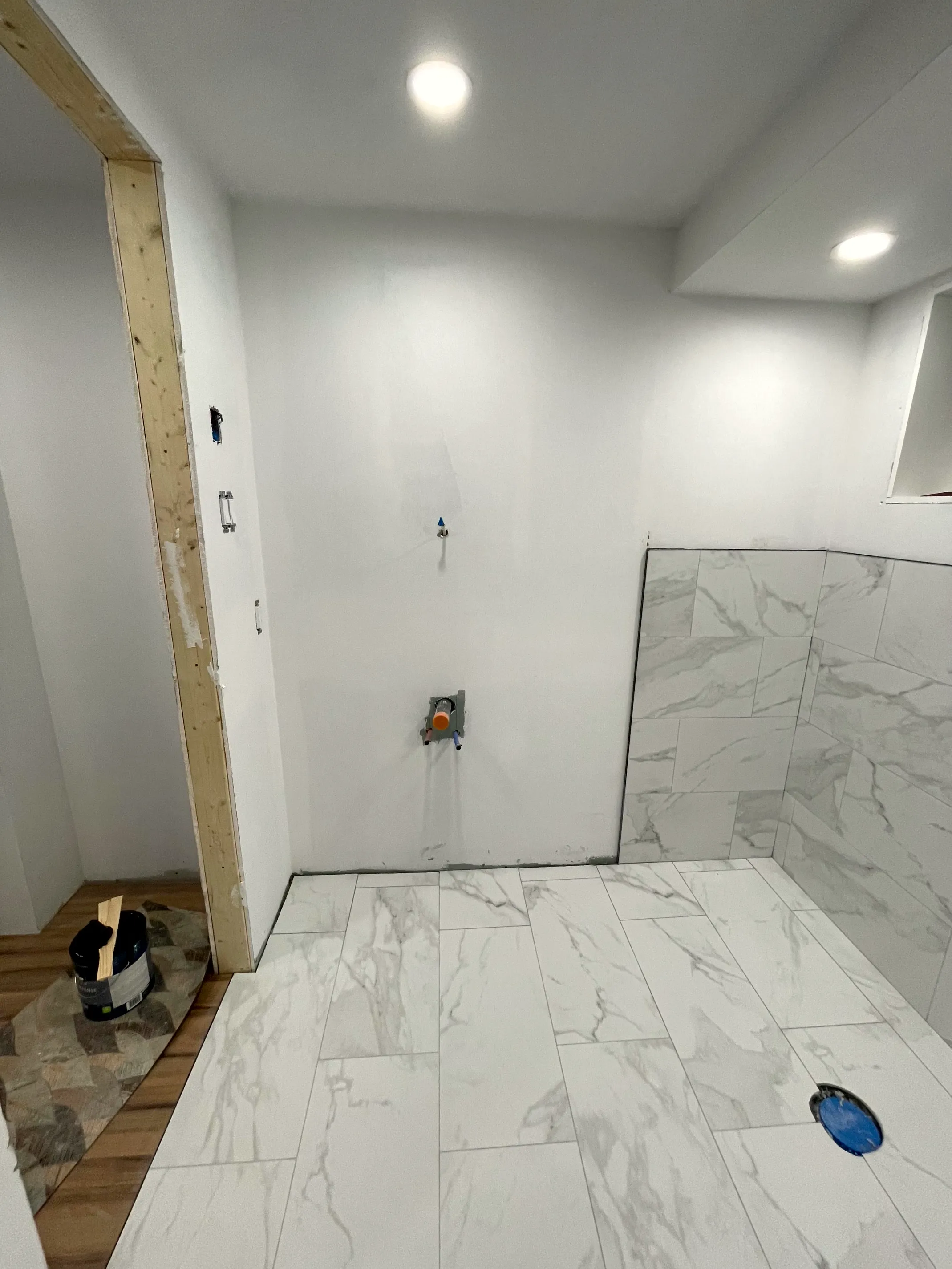 Bathroom with floor tile down, light walls, a shower valve set and one wall partly clad in stone-look tile.