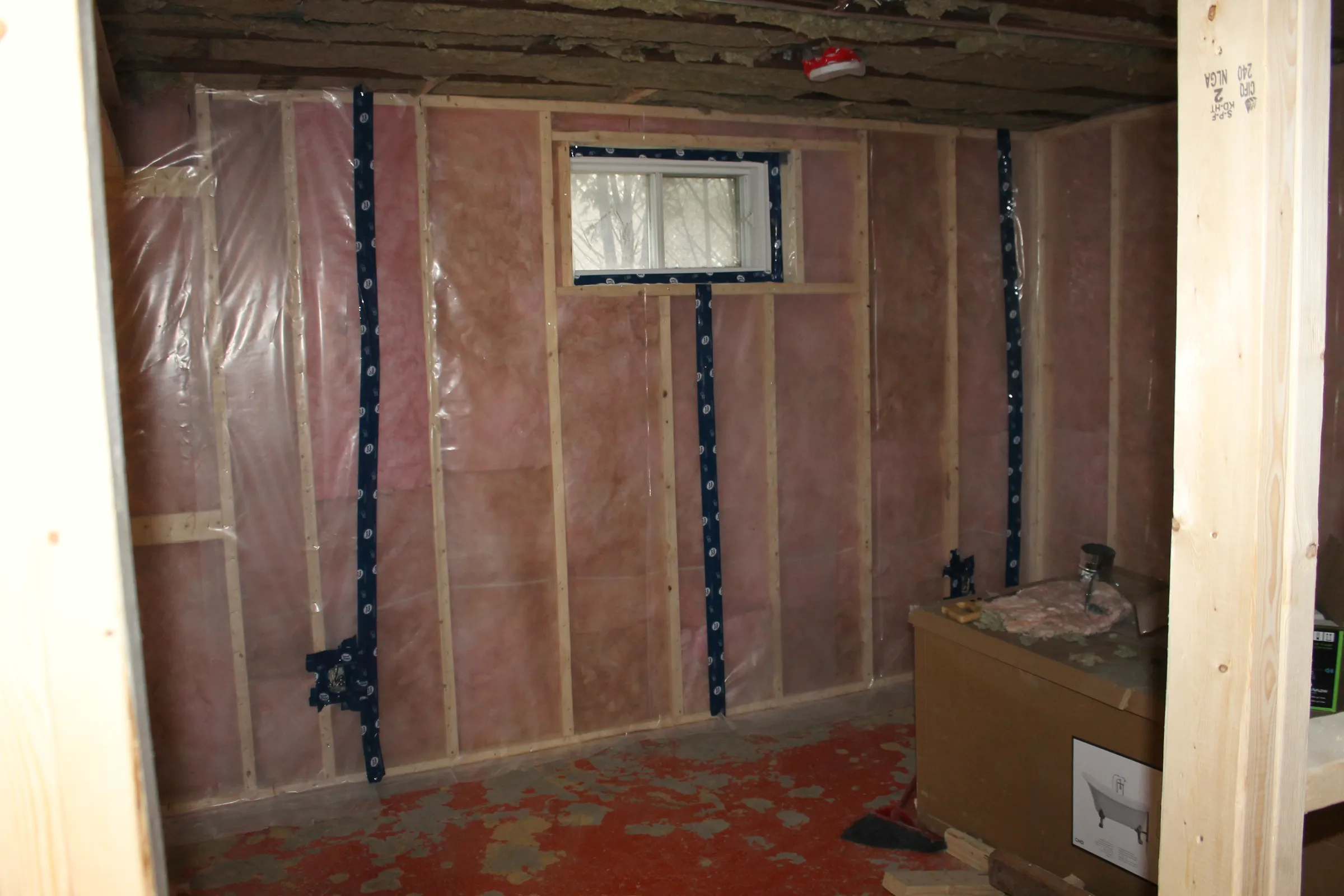 Basement wall framed with insulation and a clear vapour barrier over the studs, taped seams and a small window.