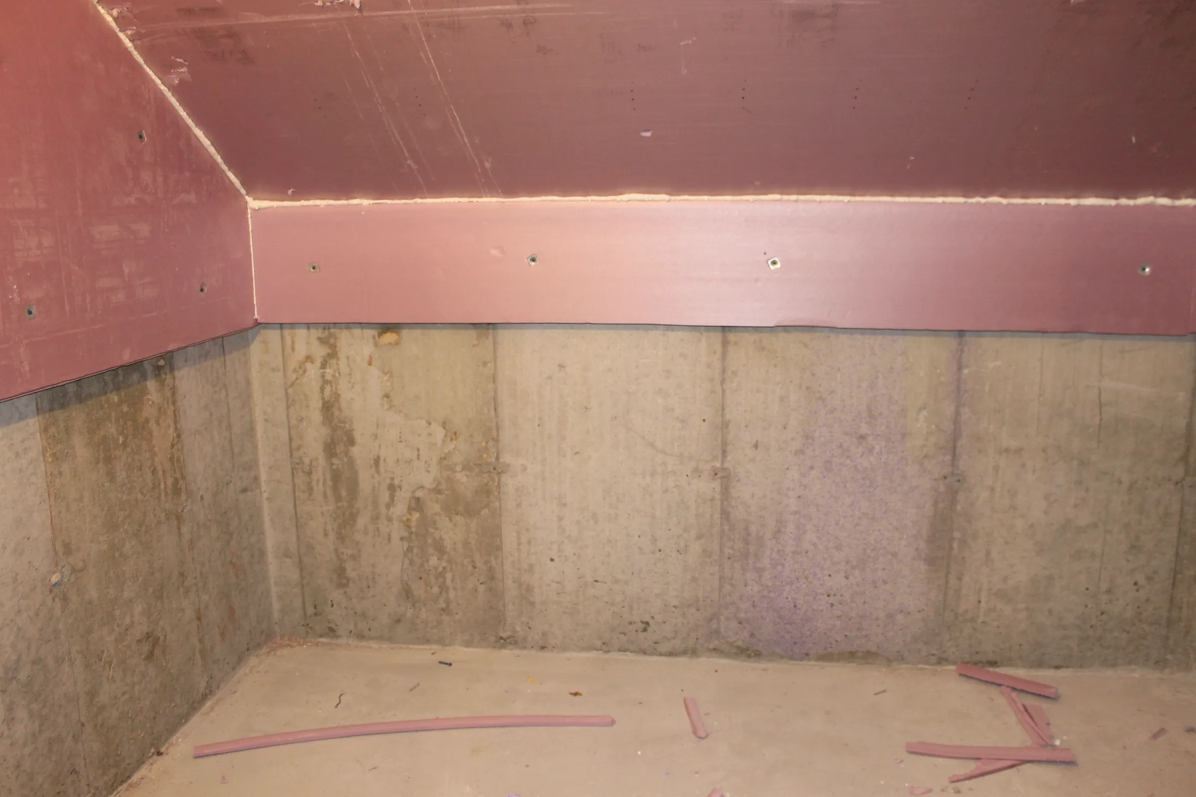 Basement concrete foundation wall with a rigid foam insulation panel fastened along the top edge.
