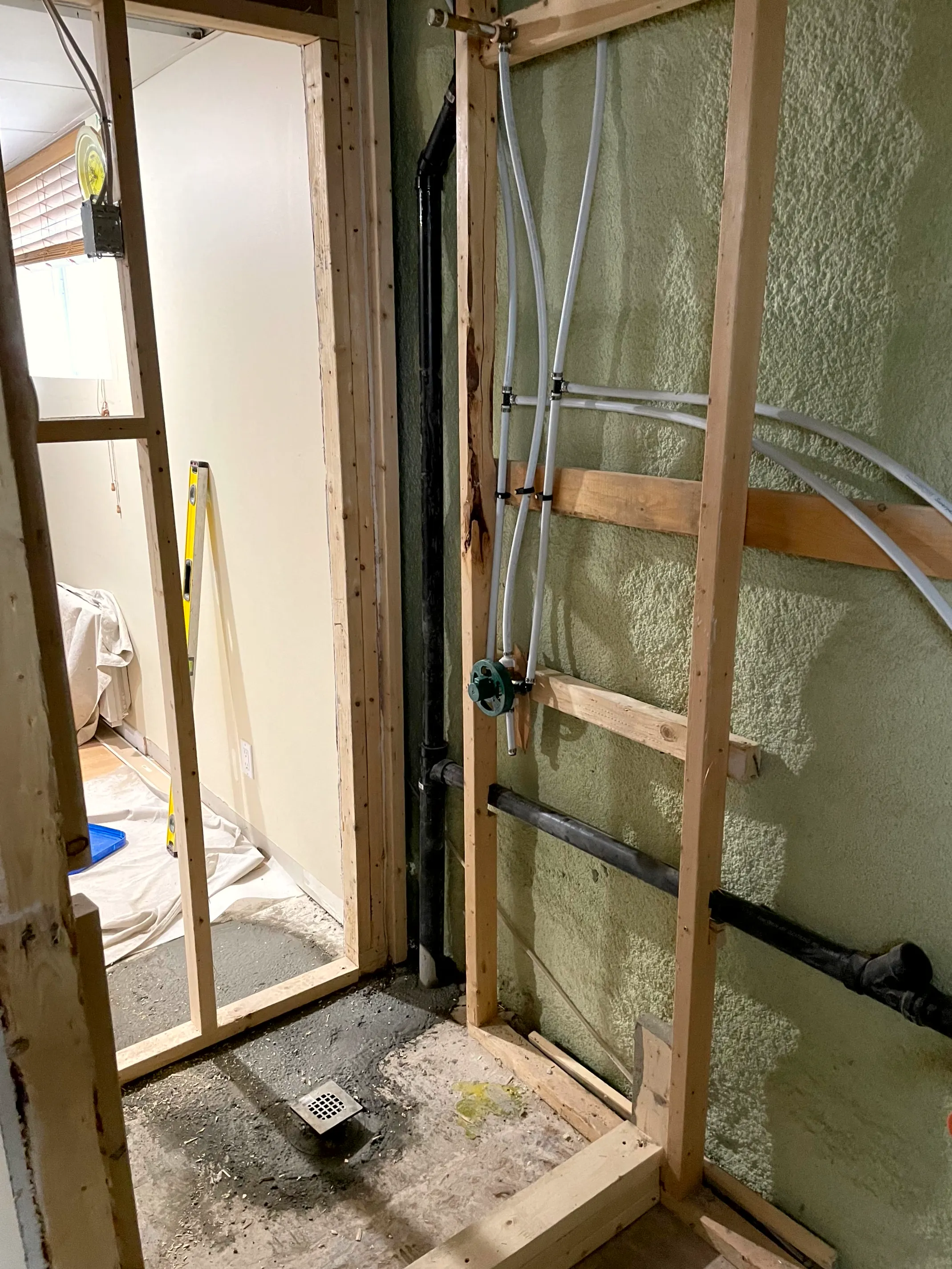 Bathroom framing with the shower valve set, supply lines run, and a shower drain in the floor.