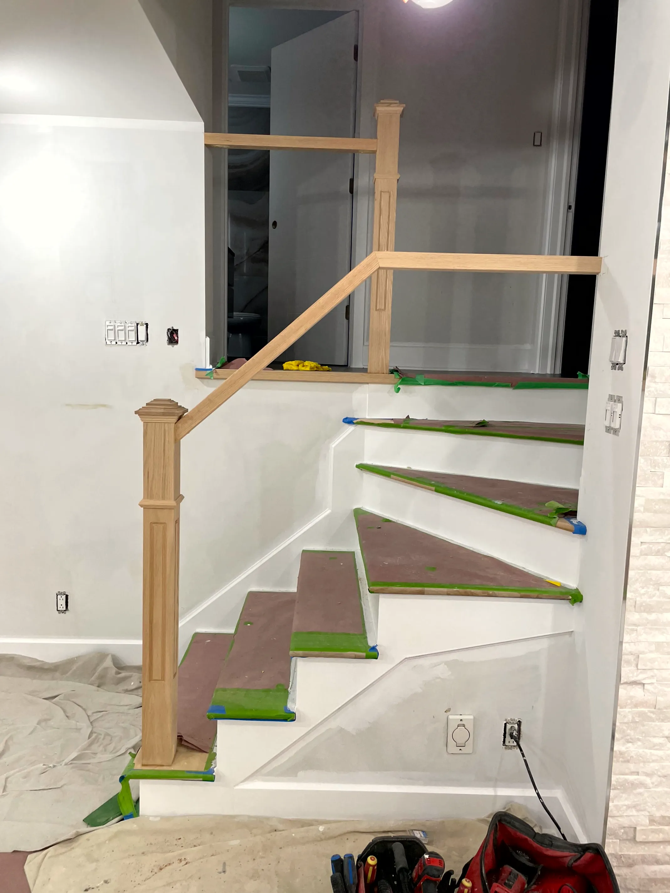 Wood handrail, newel post, and railing set around a stair opening, treads paper-covered.