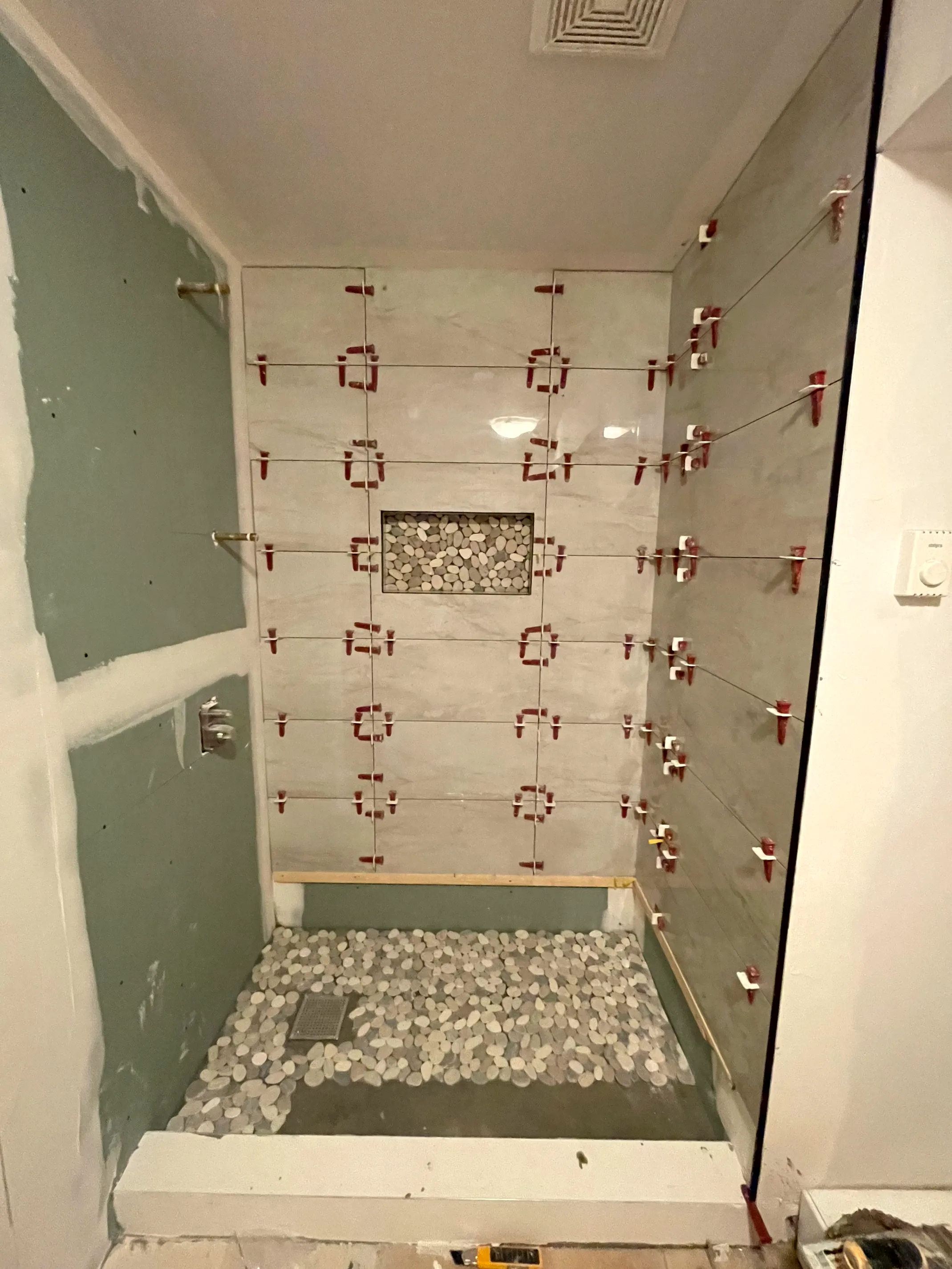 Shower wall tile set with leveling clips, a pebble-mosaic niche, and a pebble-mosaic floor.