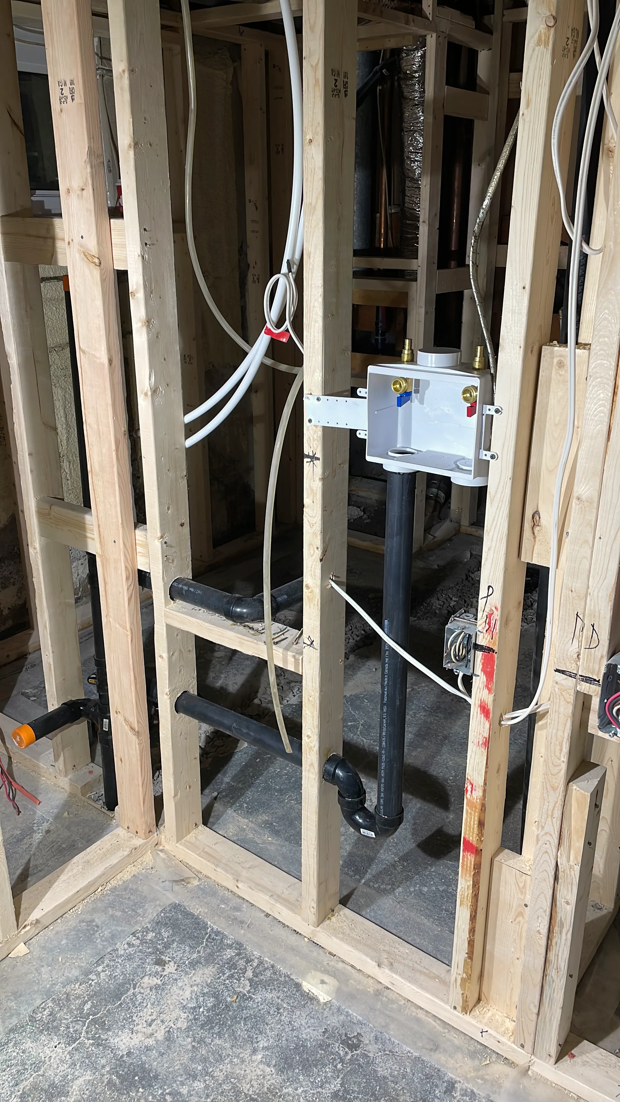 Laundry wall framing with a recessed washer box, supply lines, and black drain pipes.