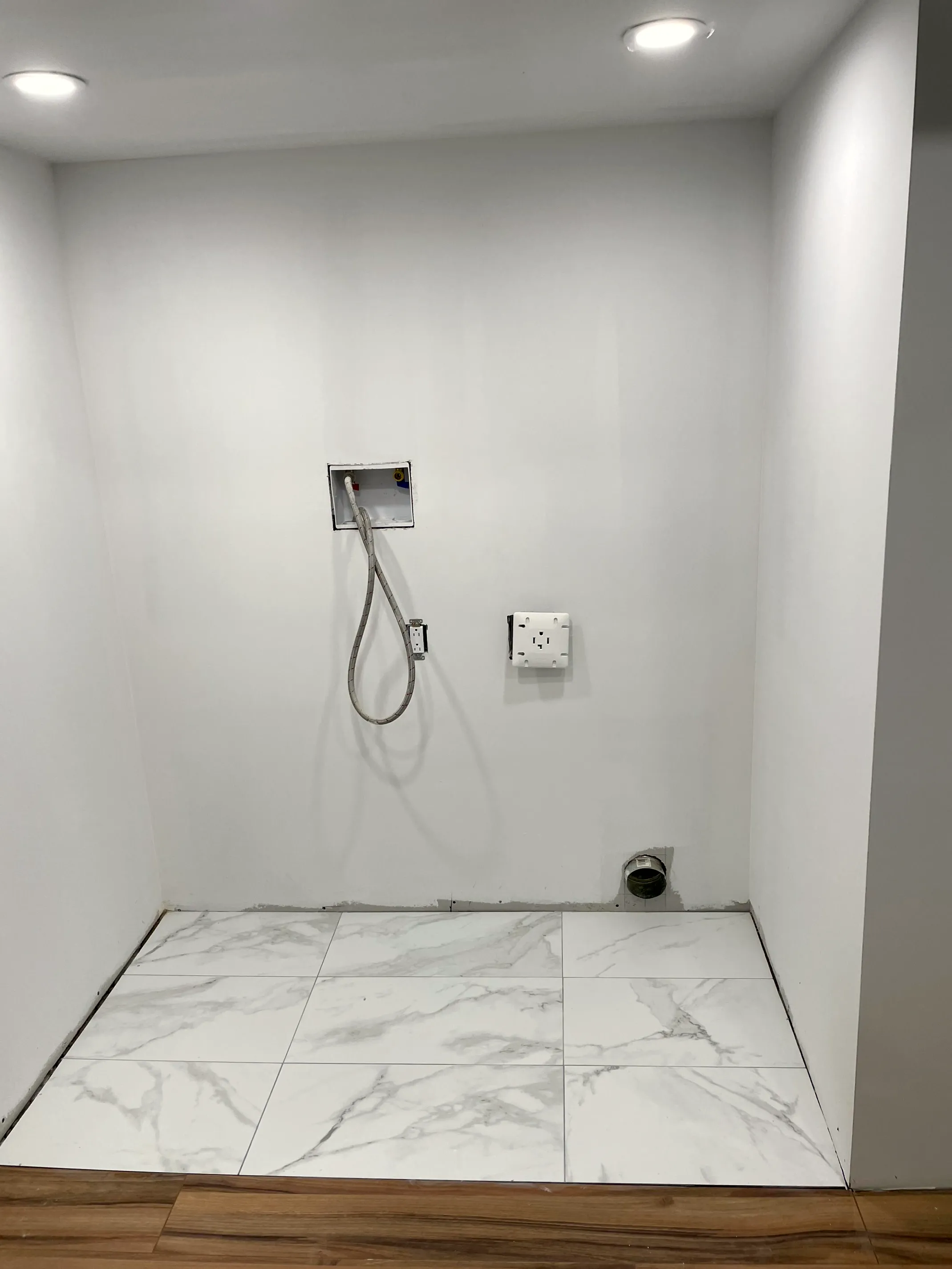Laundry alcove with a recessed washer box, a dryer vent, and a tile floor.