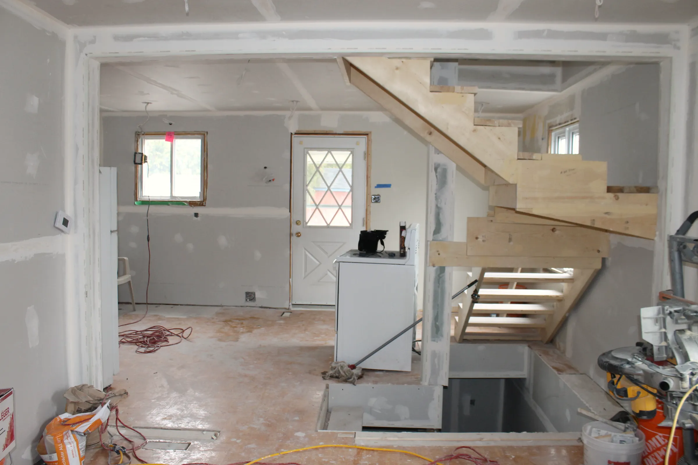 Open interior with taped drywall, a new wood staircase, and a basement stair opening below.