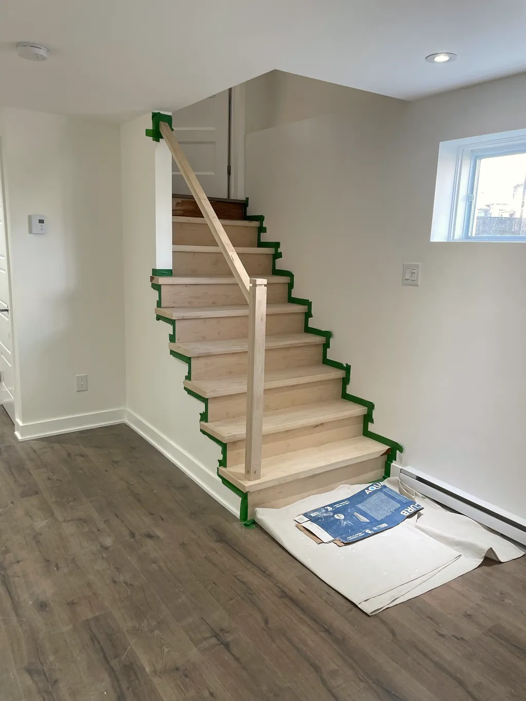 New wood staircase with taped edges, wood-look plank floor, and a baseboard heater along the wall.